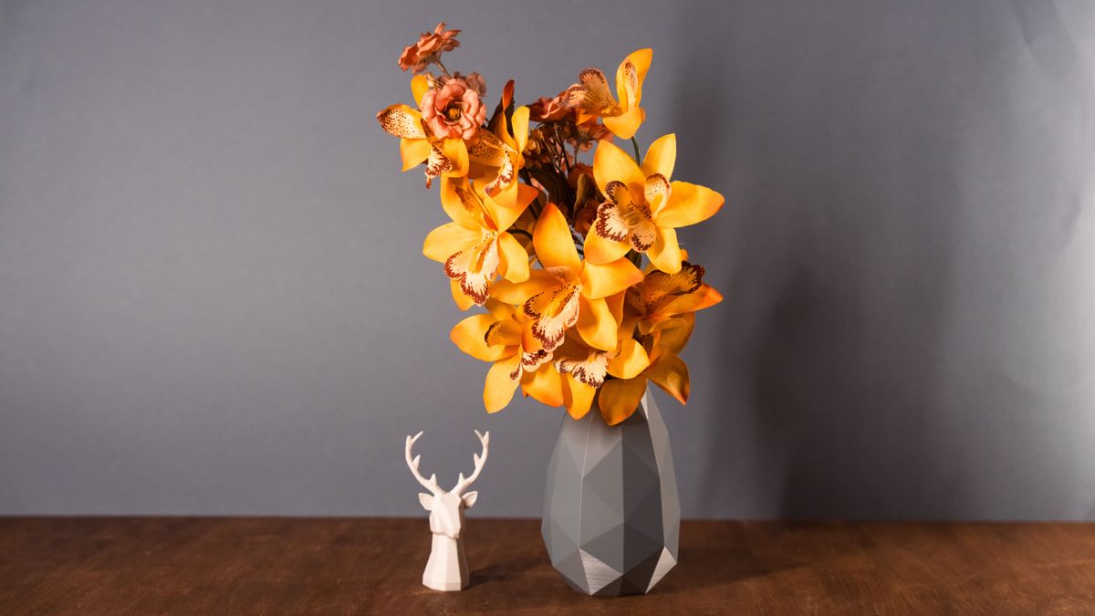 Vaso grigio low-poly con fiori e una testa di cervo stilizzata in bianco